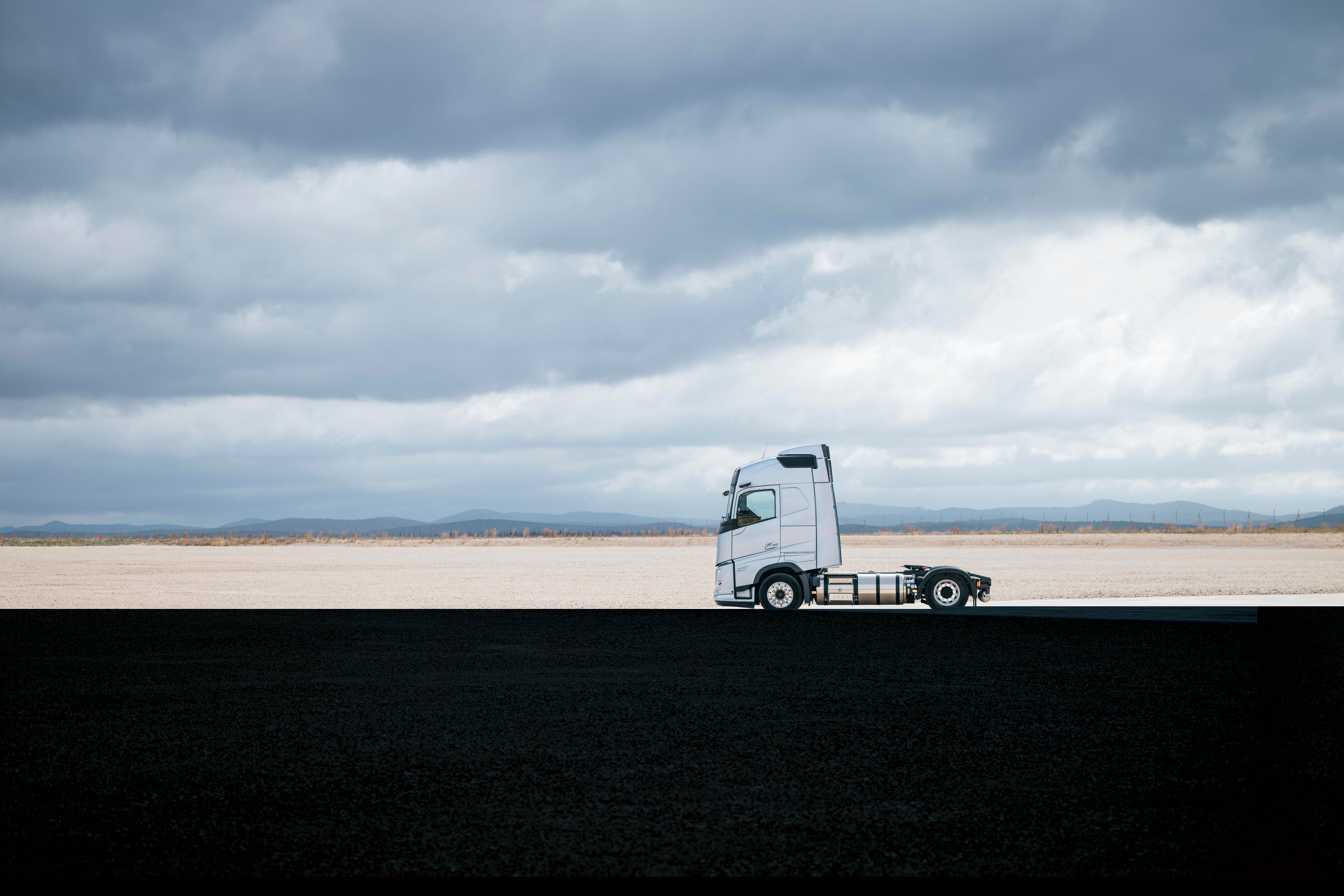 Vista lateral de un camión Volvo aparcado ante un amplio paisaje abierto bajo un cielo nublado, con un entorno espacioso y unas vistas minimalistas.